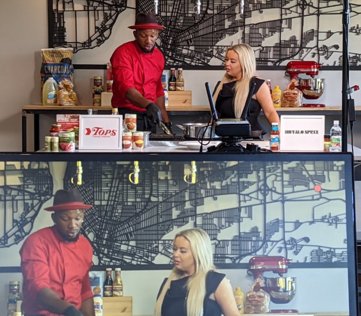 Bryan and Young in the demo kitchen, with computer monitor in front displaying the same image of them