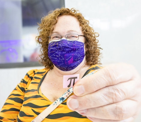 Mathematics Chair and Associate Professor wearing a math-equation mask and holding the symbol for Pi