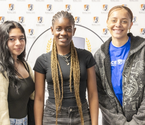 Three smiling students pose in front of a Buffalo State backdrop