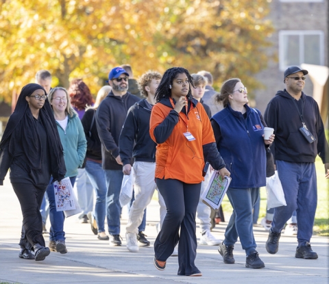 A student guide wearing an orange Buffalo State T-shirt guides a small group on a campus tour on a sunny fall day
