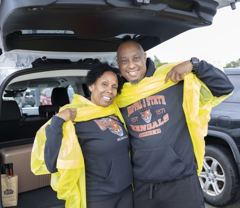 Smiling couple raising yellow rain slickers to show Buffalo State sweatshirts underneath