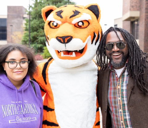 A female student and a male guardian pose with the Benji Bengal mascot