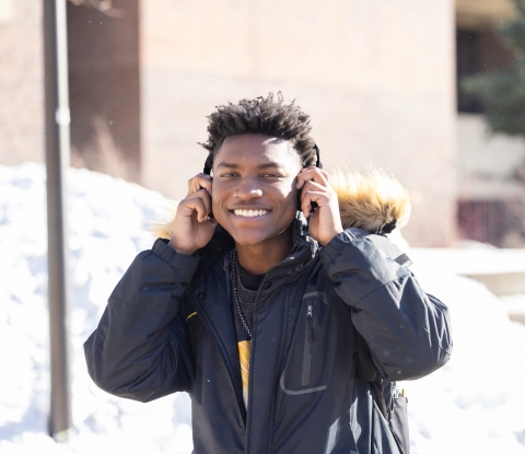 A student walks on campus in the snow smiling