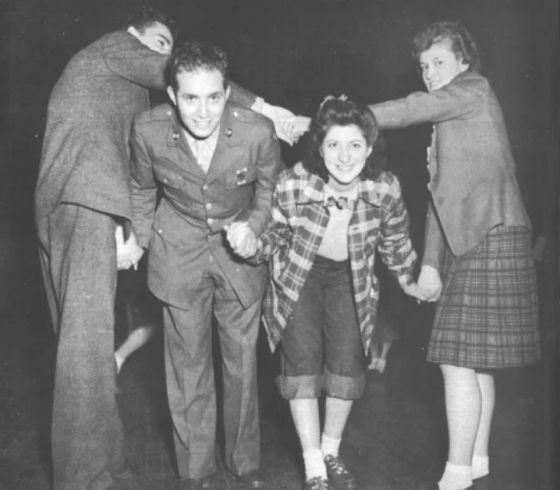 Service man in uniform and woman holding hands and ducking under the locked arms of a second couple