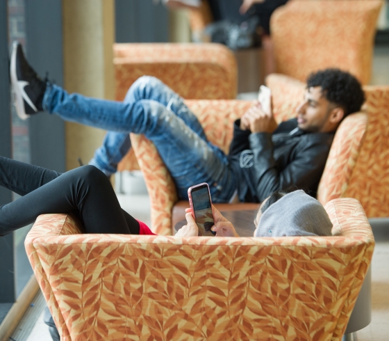 Students on smart devices lounging on chairs in library
