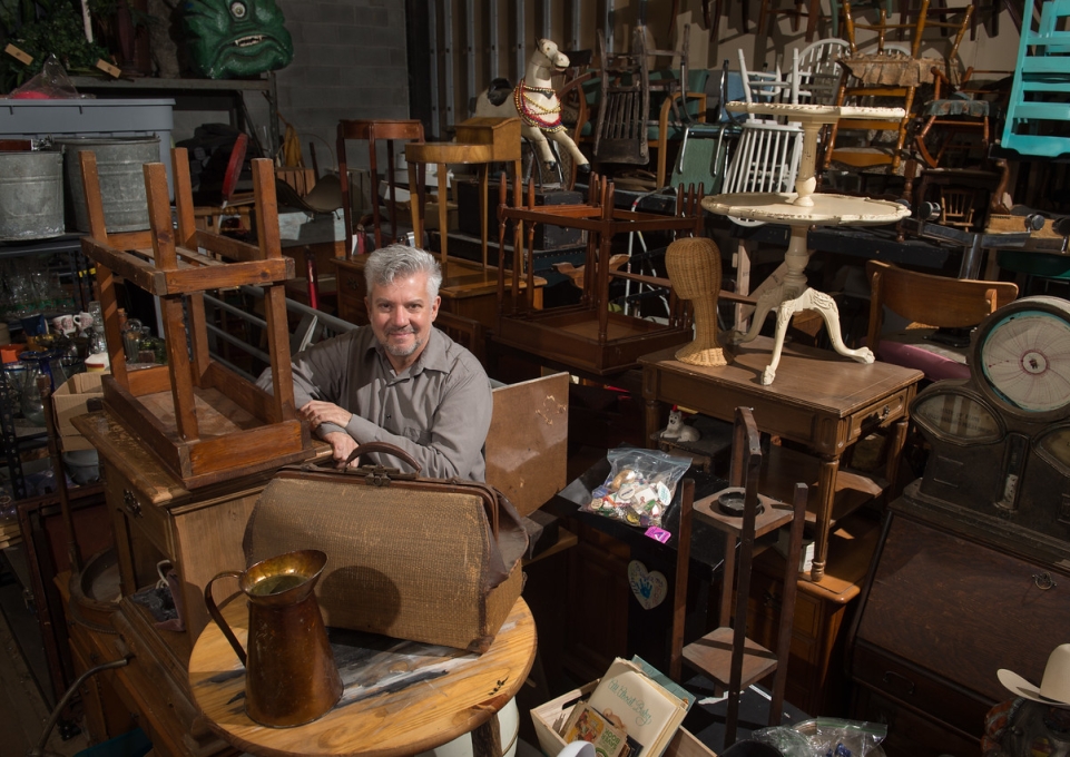 David Butler standing amid warehouse full of furniture and other set design props
