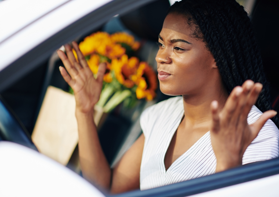 Young woman behind the wheel of a car gestures in a frustrated way