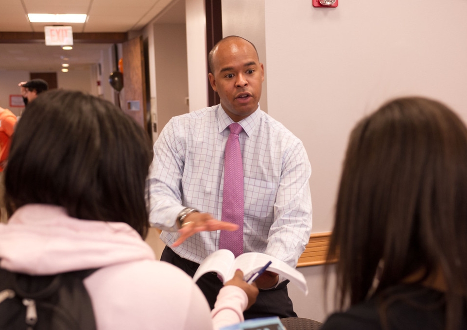 Black male wearing shirt and tie explaining something to two students