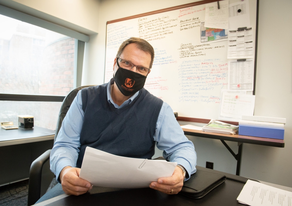 Kris Kaufman sitting at his desk in front of the large white board
