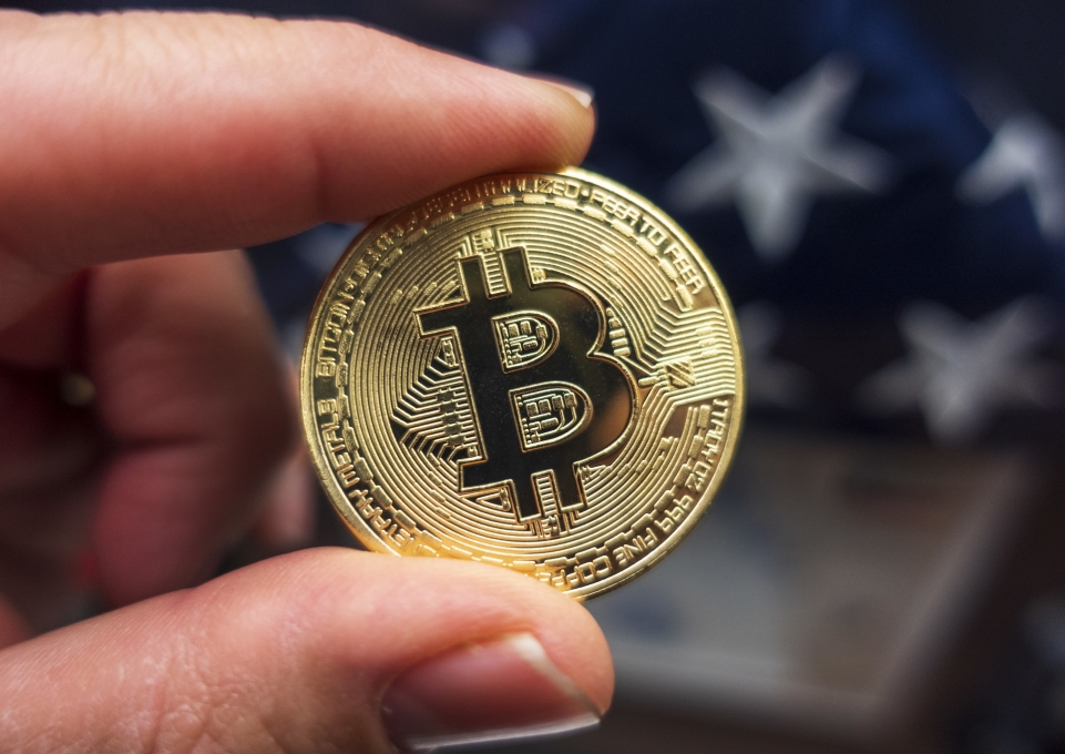 Closeup of a single bitcoin held between thumb and forefinger