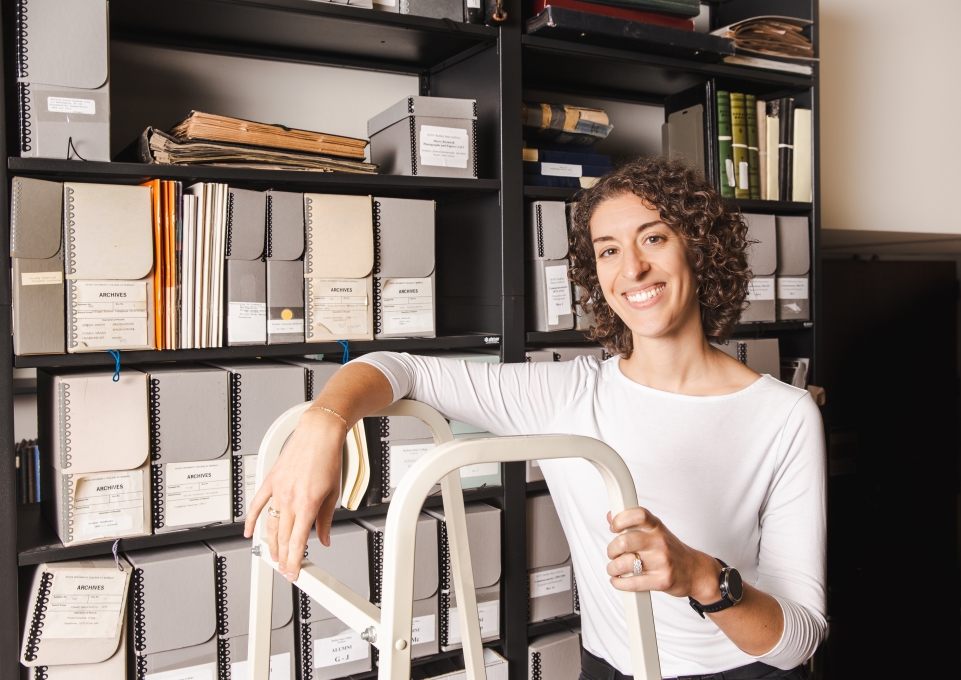 Hope Dunbar standing in front of archives stacks