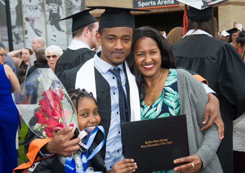 Graduate in cap and gown outside the Sports Arena hugging his family