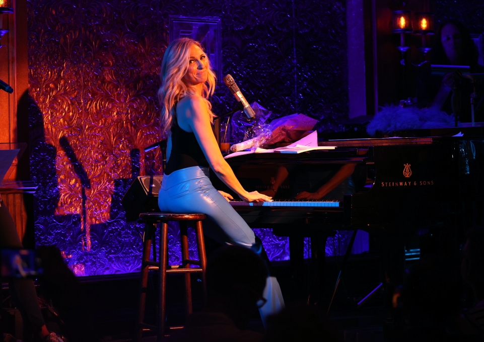 Debbie Gibson seated at the piano looking backward over her shoulder
