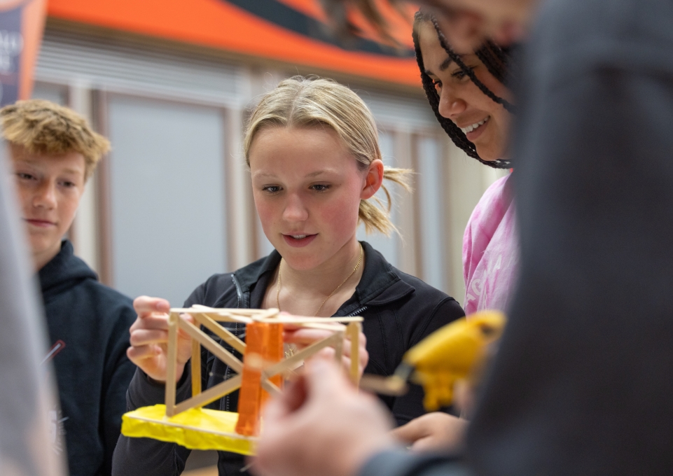 A group of students work on building a bridge with popsicle sticks