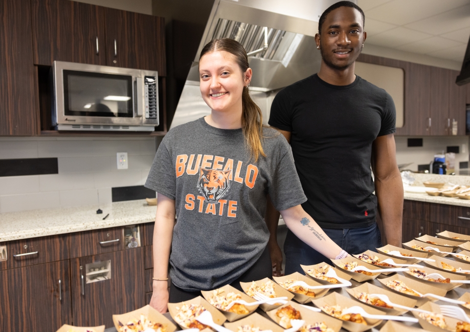 Students behind table with portioned plates of BBQ chicken and coleslaw