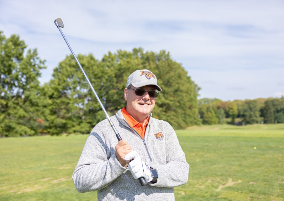A man wearing Buffalo State apparel and holding a golf club