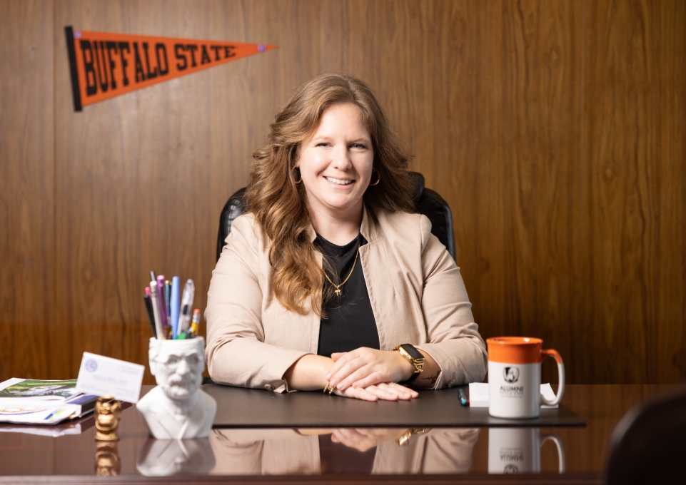 Sarah Bonk sitting at her desk with a Buffalo State pennant and mug in the background